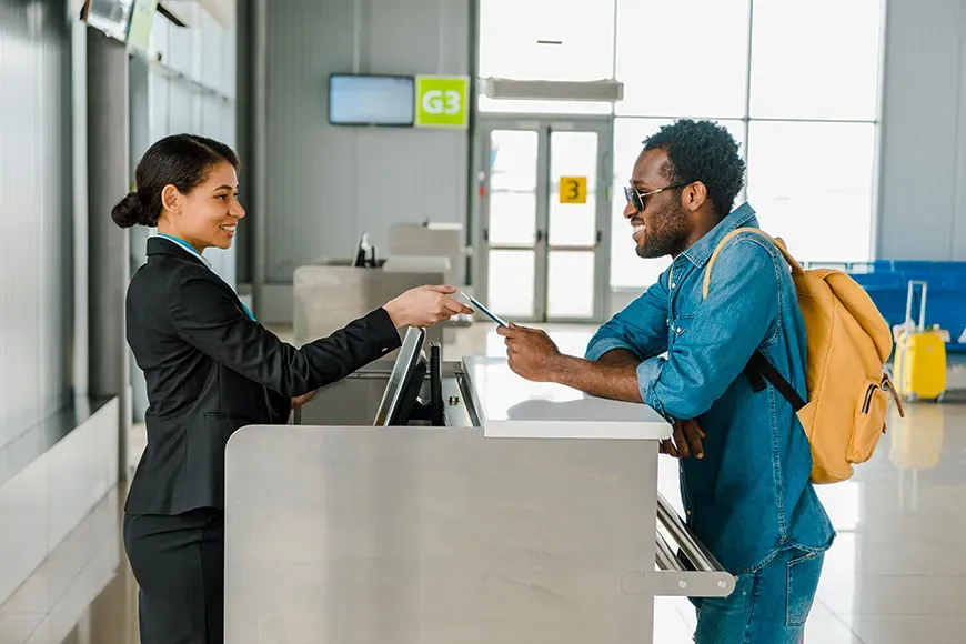 smiling african american airport worker taking passport and air ticket from tourist with backpack